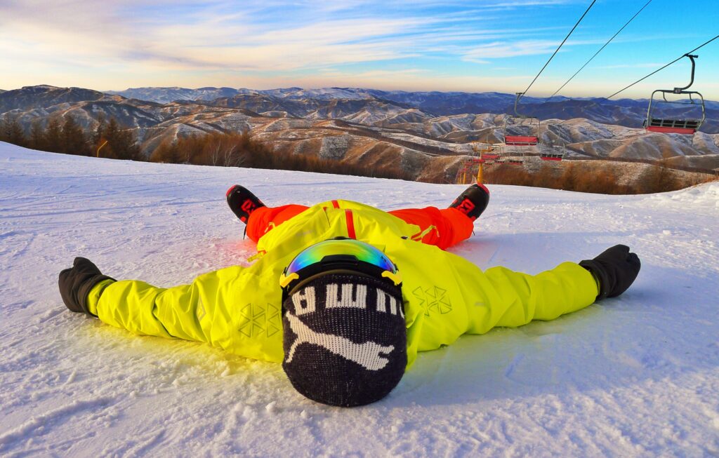 Snowboarder_Laying_On_Snow_With_MountainRange_In_Background